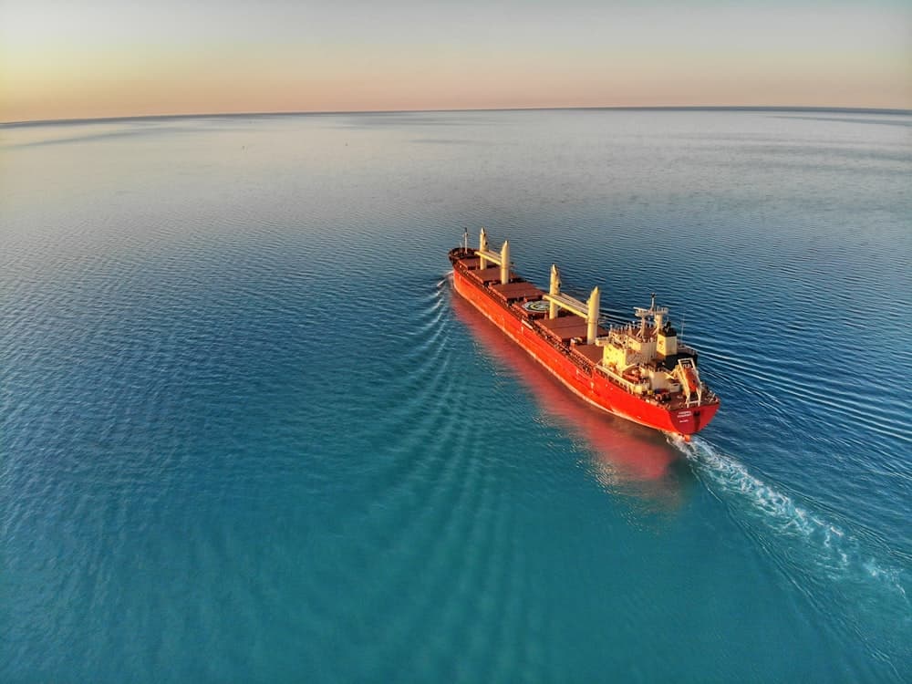 Red-hulled dry-bulk carrier with deck cranes underway at sea
